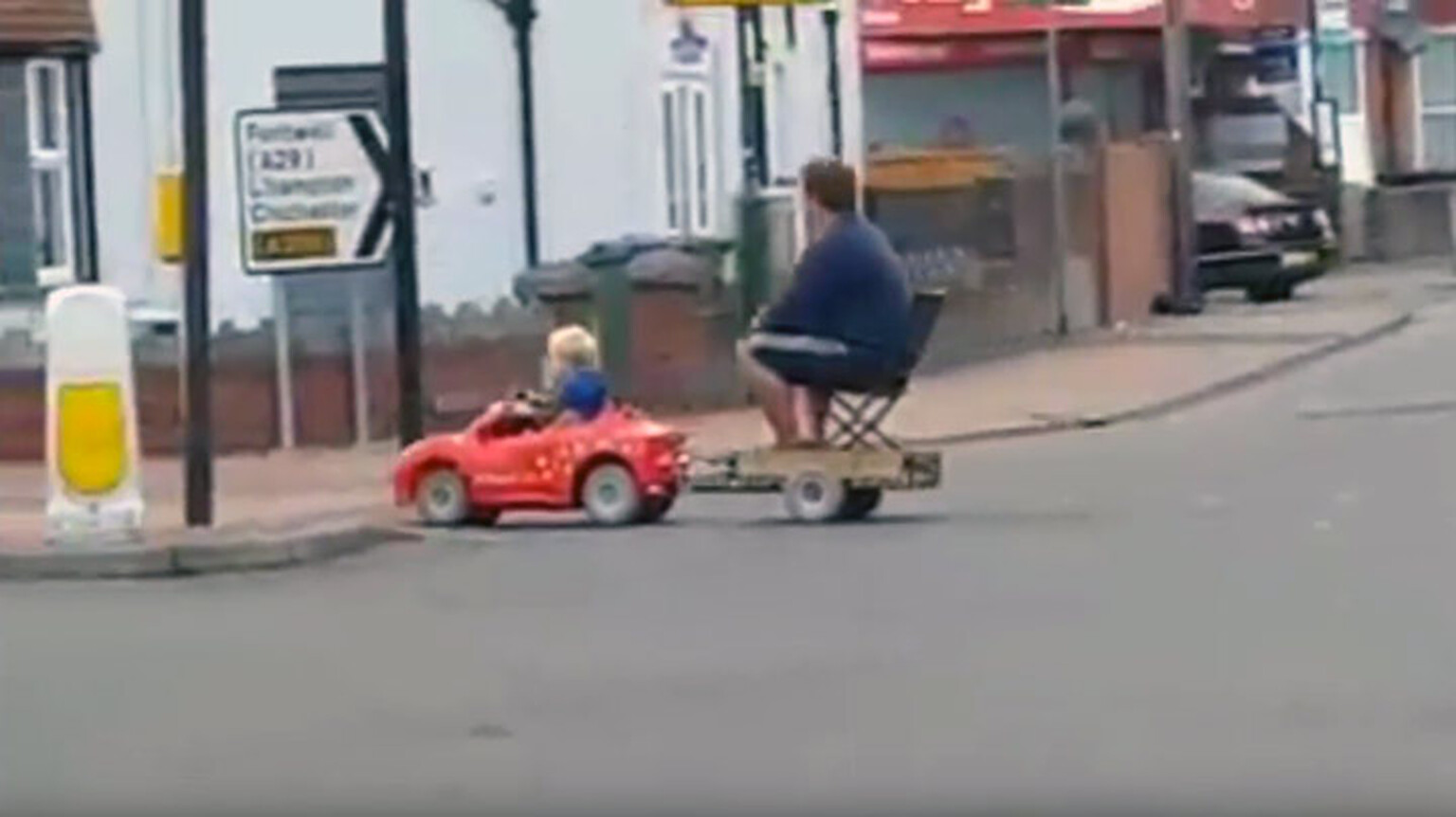Watch a young boy tow his dad home in an electric toy car