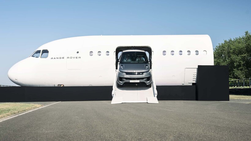 Silver prototype range rover emerging from a plane, front-on shot