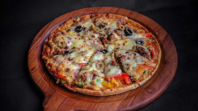Pizza with olives, mushrooms, peppers and beef on a wooden pizza peel